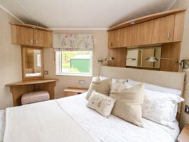 A bedroom with a bed, pillows, overhead cabinets, a window, a wall-mounted lamp, a corner desk with a mirror, and a stool at The Four Oaks Chalet in Blaich near Fort William