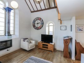 A living room with a television and clock at Eglwys St Cynfil Penrhos near Pwllheli