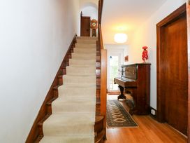 A carpeted staircase with wooden banisters next to a hallway with a wooden piano and a rug on the floor at Bryn Eithin in Borth-y-Gest near Porthmadog