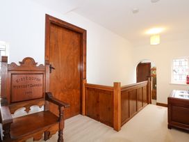 A hallway with wooden staircase railing a wooden chair with inscriptions wooden doors and a stained glass window at Bryn Eithin in Borth-y-Gest near Porthmadog