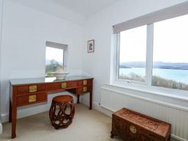 A room with a wooden desk with brass handles a matching carved wooden stool a ceramic pitcher and basin on the desk and a carved wooden chest near a window with a view of water and hills at Bryn Eithin in Borth-y-Gest near Porthmadog