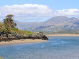 A coastal scene with a sandy beach a rocky cliff a grassy area with trees and mountains in the background at Bryn Eithin in Borth-y-Gest near Porthmadog