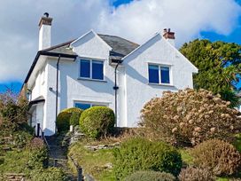 A white two-story house with chimneys and shrubs in front at Bryn Eithin in Borth-y-Gest near Porthmadog