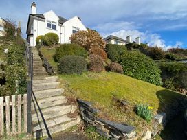 A white house with a stone staircase leading up a grass hill with bushes and a wooden gate at Bryn Eithin in Borth-y-Gest near Porthmadog