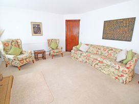 A living room with floral patterned sofa and armchairs with green cushions and a wooden door at Bryn Eithin in Borth-y-Gest near Porthmadog