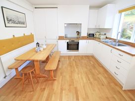A kitchen with wooden flooring white cabinets wooden table with benches and a stool at Bryn Eithin in Borth-y-Gest near Porthmadog