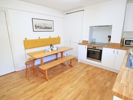 A kitchen with a wooden dining table and bench stools white cabinets and an oven at Bryn Eithin in Borth-y-Gest near Porthmadog