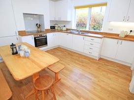 A kitchen with wooden floor and table white cabinets and a window at Bryn Eithin in Borth-y-Gest near Porthmadog
