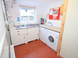 A utility room with a washing machine fridge sink cabinets fire extinguishers and a bulletin board at Bryn Eithin in Borth-y-Gest near Porthmadog