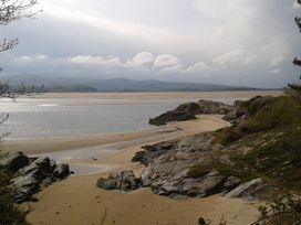A sandy beach with rocks and water under a cloudy sky at Bryn Eithin in Borth-y-Gest near Porthmadog
