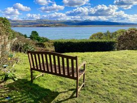 A wooden bench on grass facing a body of water with hills and clouds in the background at Bryn Eithin in Borth-y-Gest near Porthmadog