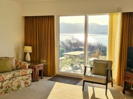 A living room with a floral sofa and armchair facing sliding glass doors showing a picnic table and water view at Bryn Eithin in Borth-y-Gest near Porthmadog