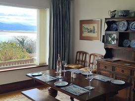 A dining room with a wooden table set for four seats near a large window with a scenic view at Bryn Eithin in Borth-y-Gest near Porthmadog