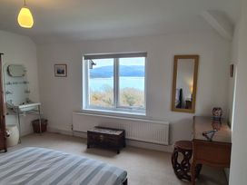 A bedroom with a bed striped bedspread a wooden chest a sink a mirror and a window showing a lake and mountains at Bryn Eithin Borth-y-Gest near Porthmadog