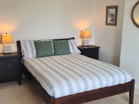 A bedroom with a bed with striped bedding and green pillows between two black nightstands with lamps at Bryn Eithin in Borth-y-Gest near Porthmadog