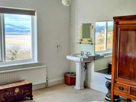 A room with a white pedestal sink beside a window and a wooden chest and cabinet at Bryn Eithin Borth-y-Gest near Porthmadog