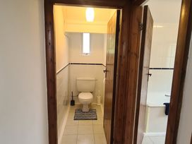A bathroom with a toilet a small window a toilet brush a striped rug and a bathtub visible through a wooden door at Bryn Eithin in Borth-y-Gest near Porthmadog
