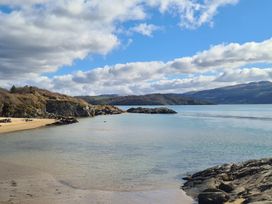 A coastal scene with a sandy beach rocks hills and clouds over water at Bryn Eithin in Borth-y-Gest near Porthmadog