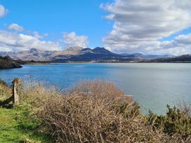 A body of water with bushes and grass in the foreground and mountains in the background at Bryn Eithin Borth-y-Gest near Porthmadog