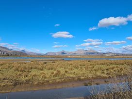 A landscape with grass, a body of water, distant mountains, and a clear sky with clouds at Bryn Eithin in Borth-y-Gest near Porthmadog