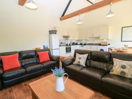 An open plan living room and kitchen with two black leather sofas with cushions and a wooden coffee table with a white vase and purple flowers at The Old Stables in Winterborne Stickland