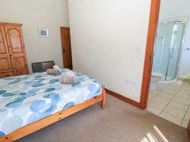A bedroom with a wooden bed with a blue and white duvet next to a wooden wardrobe and a door leading to a bathroom with a shower at The Old Stables in Winterborne Stickland