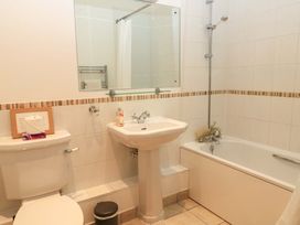 A bathroom with a toilet a pedestal sink a mirror a bathtub with a showerhead and tiled walls at The Old Stables in Winterborne Stickland