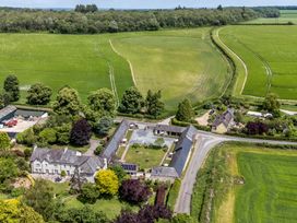 An aerial view of a house and barns surrounded by fields and trees at Corner Barn Winterborne Stickland