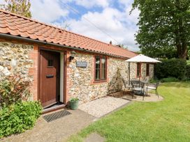 A stone cottage with a red tiled roof and outdoor table with umbrella in a garden at Moonlight Cottage in Coltishall