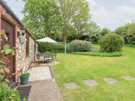 A garden with a stone and brick cottage patio table chairs and umbrella and green lawn at Moonlight Cottage in Coltishall