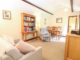 A living room with a sofa a plaid armchair a wooden bookshelf and a dining table with chairs at Moonlight Cottage in Coltishall