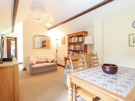A living room with a beige sofa a wooden bookshelf a dining table with chairs and a bowl on top at Moonlight Cottage in Coltishall