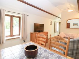 A room with a table and chairs near a window a TV on a wooden cabinet a sofa with cushions and a mirror on the wall at Moonlight Cottage in Coltishall