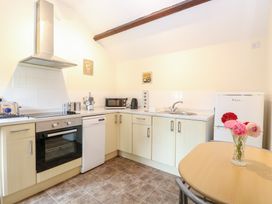 A kitchen with light wood cabinets a built in oven microwave toaster kettle small fridge and round table with flowers at Moonlight Cottage in Coltishall