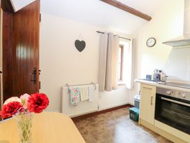 A kitchen with a wooden door a table with flowers on it an oven a toaster and a window with curtains at Moonlight Cottage in Coltishall