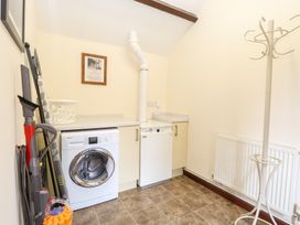 A utility room with a washing machine a dishwasher an ironing board vacuum cleaner coat rack and a laundry basket at Moonlight Cottage in Coltishall