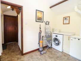 A laundry room with washing machine ironing board vacuum cleaner and laundry basket at Moonlight Cottage in Coltishall