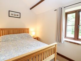 A bedroom with a wooden bed frame a patterned bedspread a bedside table with a lamp and a window with curtains at Moonlight Cottage in Coltishall