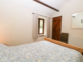A bedroom with a wooden bed, patterned bedding, a window with curtains, a wooden door, a chair, a radiator, and a wall mirror at Moonlight Cottage in Coltishall