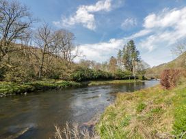 A river bordered by trees and grass at Gardener's Cottage in Llanwrthwl near Rhayader
