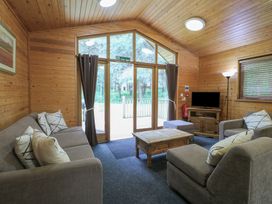 A living room with a sofa set, wooden coffee table, television on a cabinet, and large glass doors at Birch Lodge in Rosliston