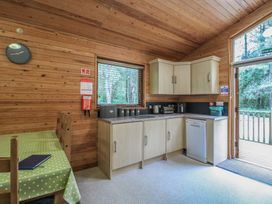 A kitchen with wooden walls, cabinets, countertop appliances, a table with chairs, and a door leading outside at Birch Lodge in Rosliston