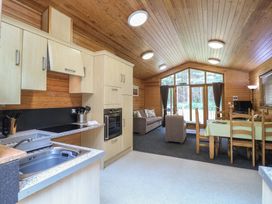A kitchen and living area with wooden panel walls and ceiling a dining table a sofa and armchair at Birch Lodge in Rosliston