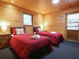 A bedroom with two single beds red bedding wooden walls and two bedside tables with lamps at Birch Lodge in Rosliston