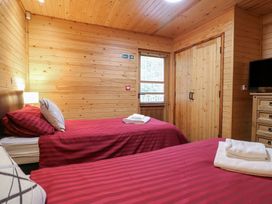 A bedroom with two single beds with red striped bedding wooden walls a window a wooden wardrobe and a chest of drawers at Birch Lodge in Rosliston