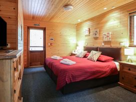 A bedroom with a double bed and red bedding wooden walls with three paintings wooden cabinets and a door at Birch Lodge in Rosliston