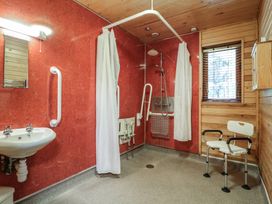 A bathroom with a shower area with white curtains a wall-mounted shower seat a sink a white chair and a window with blinds at Birch Lodge in Rosliston