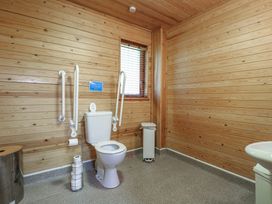 A wooden paneled bathroom with a toilet with support rails a window and a trash bin at Birch Lodge in Rosliston