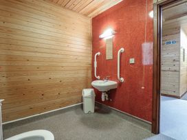 A small bathroom with wooden walls a white sink mounted on a red tiled wall a mirror above the sink grab bars a waste bin and a door leading to a hallway at Birch Lodge in Rosliston
