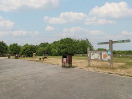 An outdoor area with a paved path grass benches trash bins a signpost and trees in the background